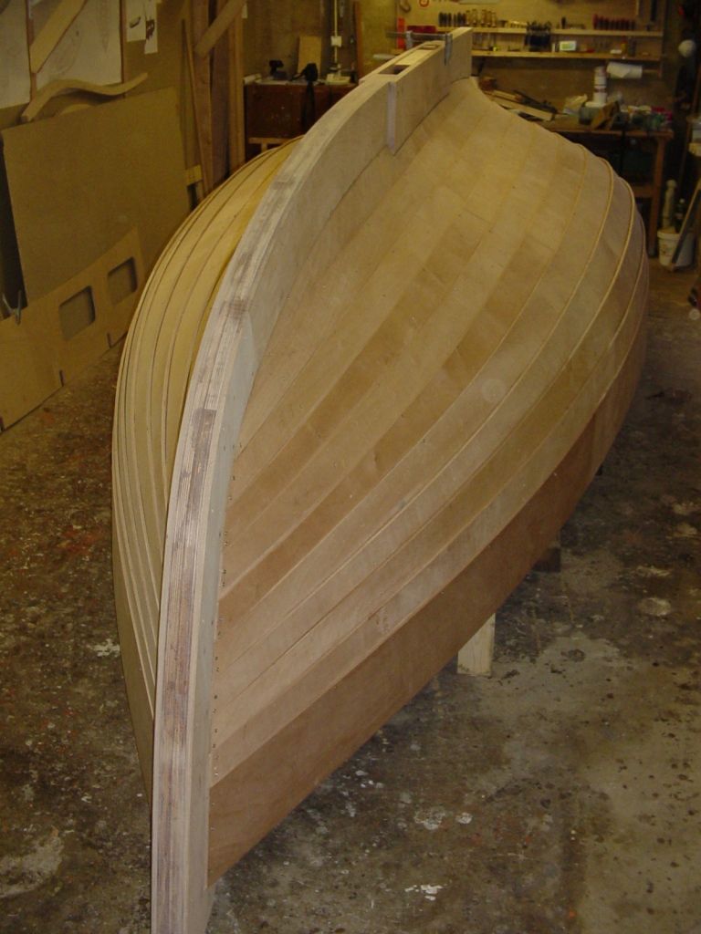 Zelfbouwromp van een houten sloep met blank houten overnaadse huidgangen in een werkplaats